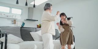 亚裔家庭小女孩和爷爷奶奶在客厅一起跳舞。孩子和老人带着笑脸运动，心情愉快。可爱的家庭和活动理念的快乐时刻