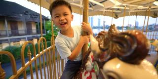 在游乐场旋转木马或旋转木马上的亚洲孩子。幸福和假日的概念
