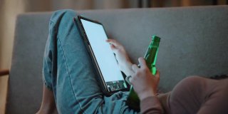 亚洲女性坐在家里的数字平板电脑沙发上喝啤酒