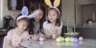 妈妈帮助两个亚裔女孩给复活节彩蛋着色