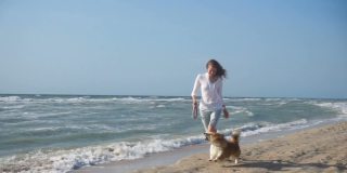 年轻的微笑女孩和柯基狗跑在海边