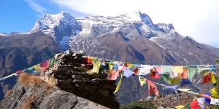 尼泊尔喜马拉雅山昆布纳姆切巴扎村的一堆石头上挂着五颜六色的佛教经幡，在风中飘扬，还有雄伟的孔德里峰。