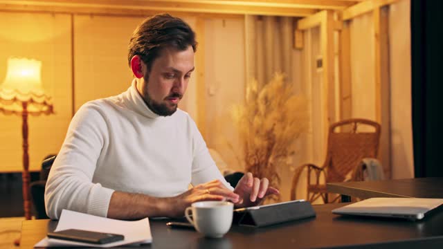 快乐的残疾人中年男子坐在轮椅上在数字平板上打字，享受使用在线应用程序，在家里的电脑上写电子书