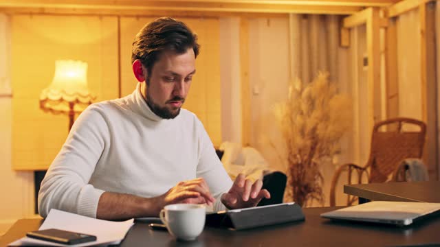 集中残疾残疾中年男子坐在轮椅上在数字平板电脑上打字，享受使用在线应用程序，在家里的电脑上写电子书