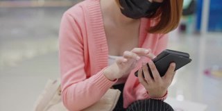 美丽的亚洲女性戴着防护口罩在商店使用智能手机，新常态概念，新冠肺炎后的人们生活方式