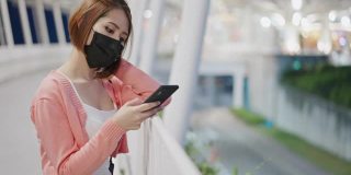 亚洲孤独女性戴着防护面罩，在商店里用智能手机