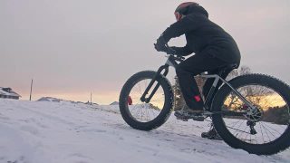 职业极限运动员骑着一辆胖胖的自行车坐在户外。骑自行车的人斜倚在冬天的雪林里。带着头盔和眼镜的大轮胎骑山地车的人。慢动作，180fps。视频素材模板下载