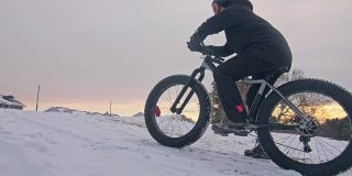 职业极限运动员骑着一辆胖胖的自行车坐在户外。骑自行车的人斜倚在冬天的雪林里。带着头盔和眼镜的大轮胎骑山地车的人。慢动作，180fps。