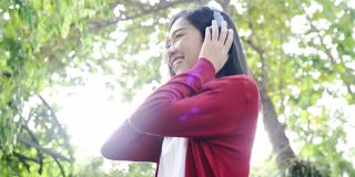 美丽的亚洲女人戴着耳机在房子的花园里听着快乐的音乐。放松，假期自由自在。好天气遮天蔽日。呆在家里的概念