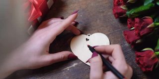 俯视图的女孩的手谁写在一个木制的心附近的一束玫瑰。情人节的概念