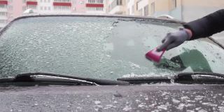 在停车场停了很长时间后，一名妇女刮去了汽车挡风玻璃上的冰。