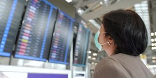 一名亚洲妇女戴着防毒面具看屏幕查看航班。