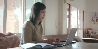 在家工作的女性员工。年轻的亚洲女人在电脑上滚动。她收到来自笔记本电脑的信息，并微笑着阅读信息。