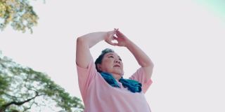 超重的资深亚洲女性在公园里做手臂和肩膀背部肌肉和脊椎伸展运动，退休生活方式健身保健，在晴天晴天锻炼，活力健康