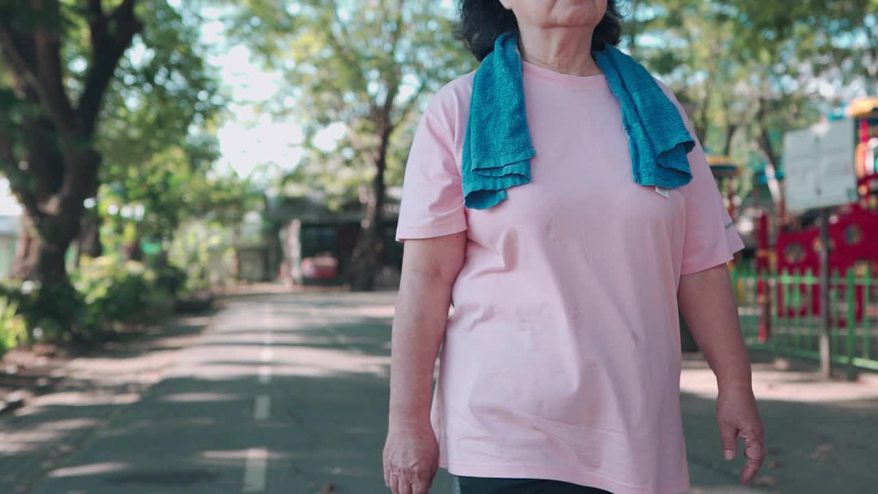 在一个阳光明媚的日子里，亚洲老年肥胖女性在公园的跑道上慢动作跑步。退休生活方式的活动。健康护理动机，脉搏血压跟踪，前瞻