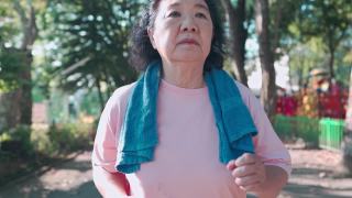 亚洲资深女性在运动公园内跑步，在阳光明媚的日子里在树荫下慢动作。退休生活方式的活动。医疗动机脉搏血压跟踪手持拍摄视频素材模板下载