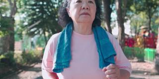 亚洲资深女性在运动公园内跑步，在阳光明媚的日子里在树荫下慢动作。退休生活方式的活动。医疗动机脉搏血压跟踪手持拍摄