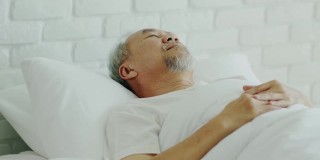 亚洲老人闭上眼睛微笑睡觉和甜蜜的梦在卧室的床上在早上感觉如此放松和舒适，保健和睡眠的概念