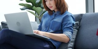 使用笔记本电脑在家工作的亚洲女性社交距离covid-19隔离冠状病毒。妇女使用笔记本电脑在家在线开会，在线学习到办公室团队会议通过电话会议