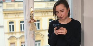 一名女子在靠近窗户的房间使用智能手机，她使用移动互联网写信息。