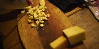 低光。女人的手在砧板上把奶酪切成小块