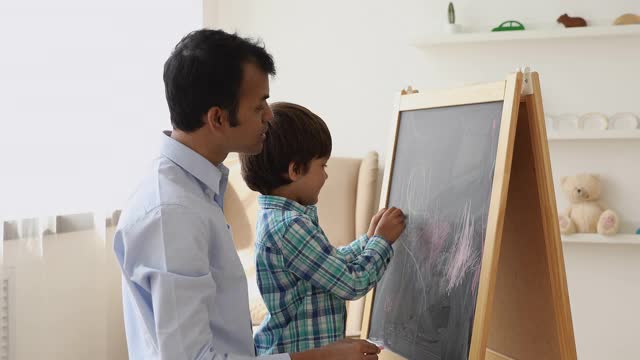 印度父亲和儿子一起用粉笔在黑板上画画