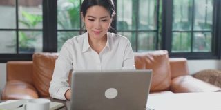 亚洲年轻女性在家工作用笔记本电脑，耳机上网与办公室同事开会。女孩避免社交距离，密切接触人群进行防护，防止病毒感染Covid-19疫情爆发