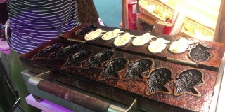 烹饪的街头食品。日式鱼饼，红豆沙馅。牛角Taiyaki日式鱼形小吃配红豆和蛋奶冻