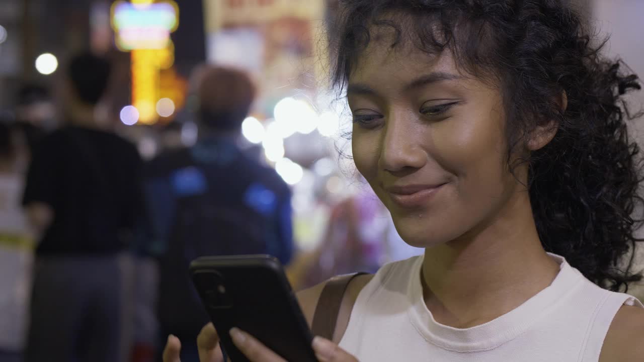 美丽的女人使用视频电话与朋友在夜间城市。她微笑着用手机打电话。