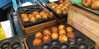 在日本的街头小吃市场，厨师从章鱼烧锅中手拿起日本小吃章鱼烧，并将其装进盒子里，在夏季节日时出售。男子烹饪什锦传统日本肉丸。