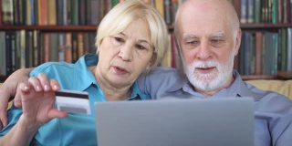 老夫妇在远程家庭办公室用笔记本电脑用信用卡在线购物。活跃的现代生活