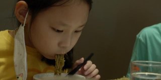快乐的亚洲女孩与家人一起在餐厅吃面条、素喜烧、涮锅或火锅，生活方式理念。