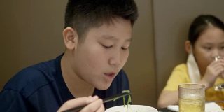 快乐的亚洲儿童与家人一起在餐厅吃素喜烧、涮涮锅或火锅，生活方式理念。