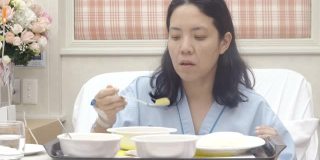 亚洲妇女病人在医院的床上吃饭