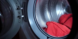 主妇将三种化学双浓缩洗衣粉颗粒扔在透明壳内的洗衣机的纺纱滚筒内，装入脏衣服进行洗涤的过程。环保清洁和去污剂的液体形状