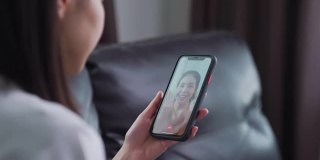 开朗美丽的亚洲女人在白色t恤做视频通话在线与朋友聊天和手触摸数码平板电脑在沙发上的相机。
