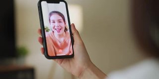 开朗美丽的亚洲女人在白色t恤做视频通话在线与朋友聊天和手触摸数码平板电脑在沙发上的相机。