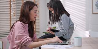 一个亚洲家庭，女商人在工作，小女孩坐在家里的桌子上。母女二人在家中被隔离的时候，在网上开会，开心的表情。
