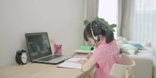 亚洲女学生视频会议电子学习与老师和同学在电脑上在家里的客厅。在家教育和远程学习，在线，教育和互联网。