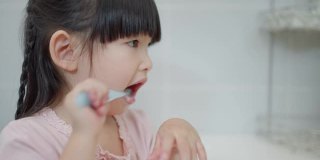 亚洲可爱的小女孩或小孩在浴室用牙刷刷牙。口腔卫生保健理念。