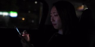 年轻的日本女子在晚上的出租车上使用智能手机