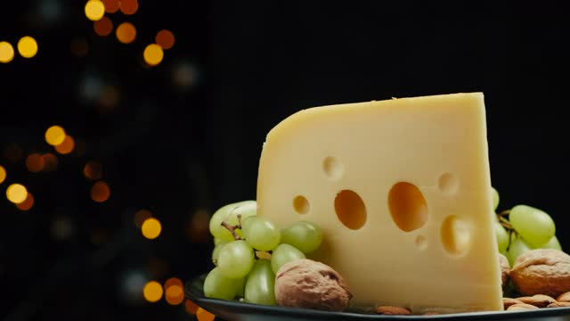 靠近中等硬的奶酪头的一部分，伊达豪达干酪帕尔马干酪放在木板上，坚果和葡萄在盘子上旋转