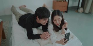 年轻夫妇躺在床上用智能手机自拍
