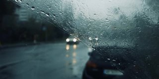 雨点落在汽车的挡风玻璃上，雨点顺着玻璃流下，汽车在道路上运动