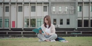 亚洲女子大学的学生坐在校园草地上看快乐和在公园看书。