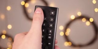 电视遥控器特写手指按下按键博克和圣诞灯在一个模糊的背景