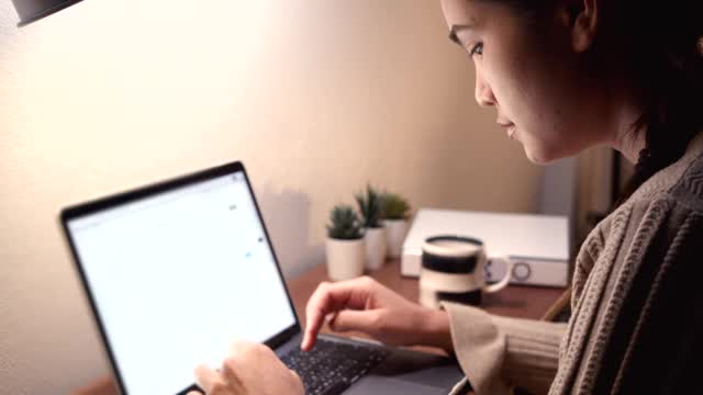 亚裔女性在家庭办公室工作。在电脑前工作。
