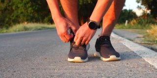 男子跑步者的近距离绑鞋带在运动运动鞋在早上日出跑步锻炼