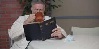 一位成熟的内科医生在医院休息室里，一边喝咖啡，一边读着他的圣经。