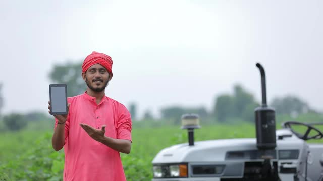 年轻的印度农民在农田里展示智能手机或平板电脑